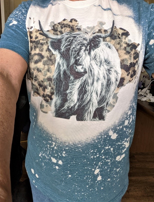 Tshirt featuring bold graphic of Highland cow on abstract background